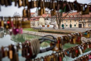A resting place on the renovated banks of the Ljubljanica River in Ljubljana, viewed between the steel wires of the Butchers' Bridge, adorned with padlocks symbolizing declarations of eternal love, a phenomenon similar to the one on the Parisian Pont des Arts.